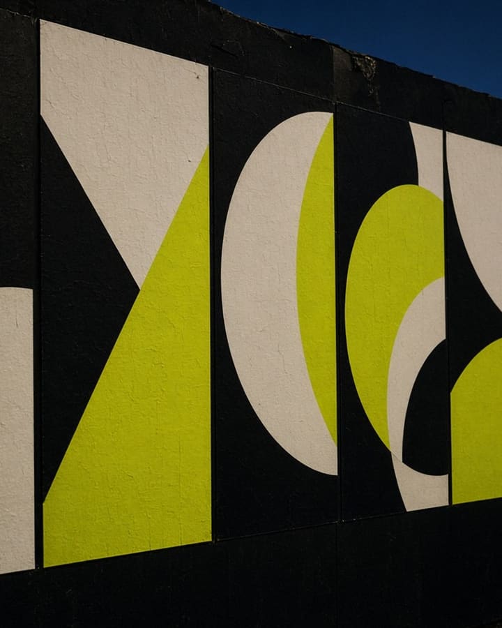Concept artwork: a wheat-pasted wall of geometric festival posters at dusk.